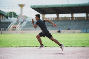 Image of a male athlete in mid-stride running on an outdoor track field with his max performance