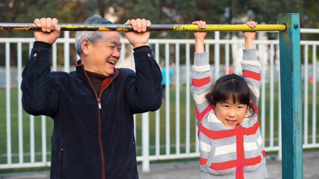 Elderly man and grandchild hanging on a monkey bar in a playground